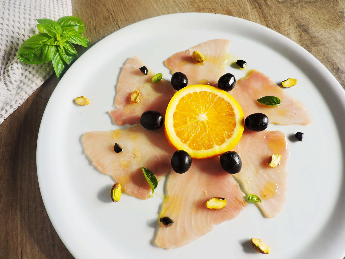 Carpaccio di tonno bianco al succo d’arancia, olive nere, pistacchi e basilico
